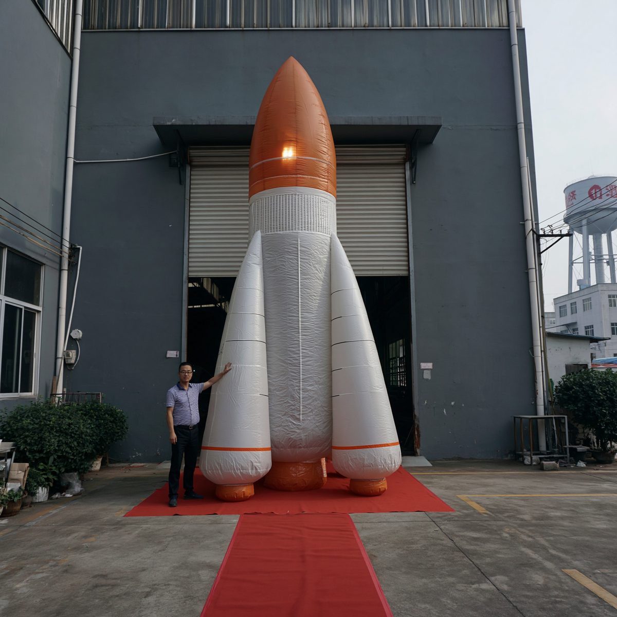A man steadying a three-meter inflatable space rocket on a red carpet outside a warehouse