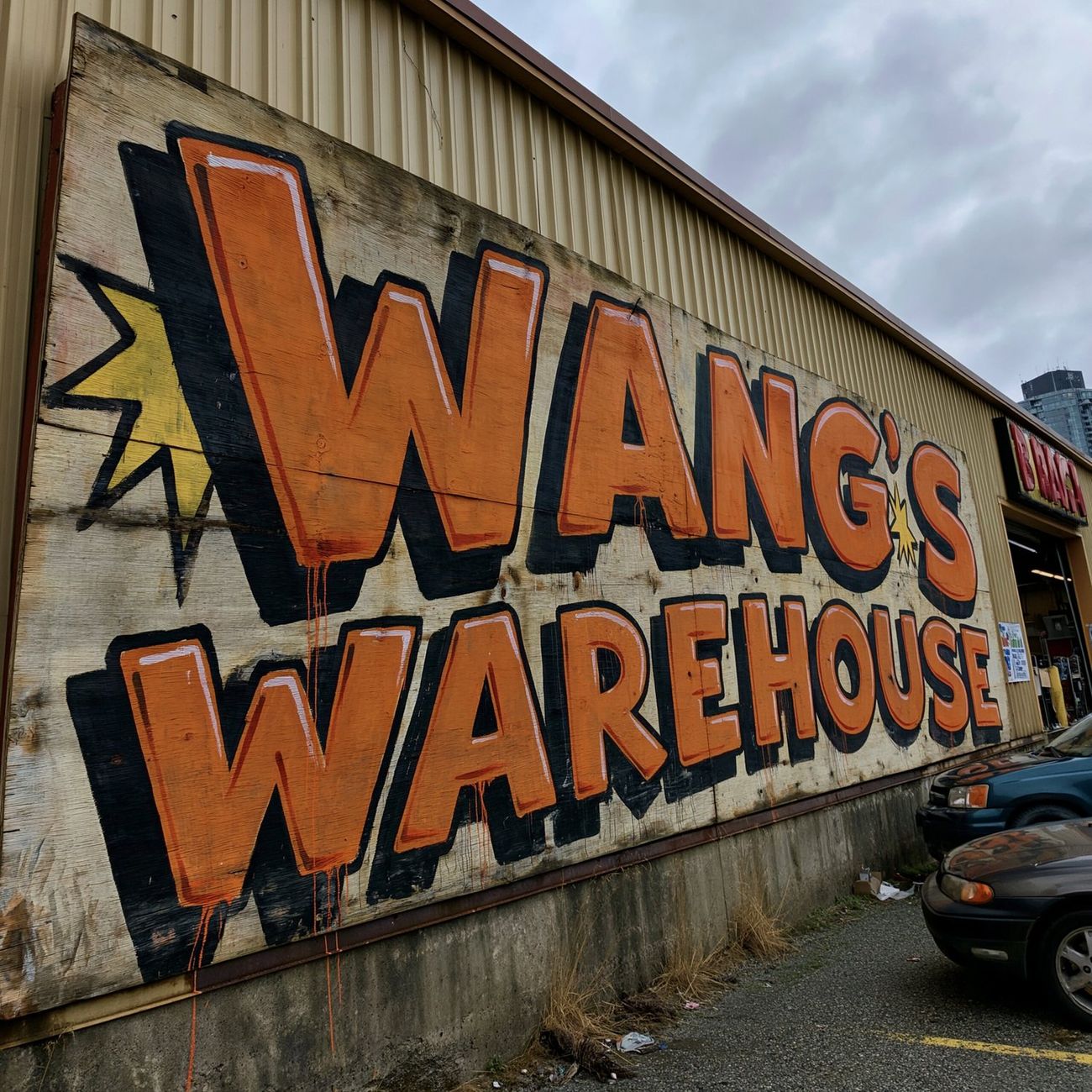 An enormous hand-painted plywood Wang's Warehouse sign on the side of a beige big-box building, orange letters with black outlines and paint drips